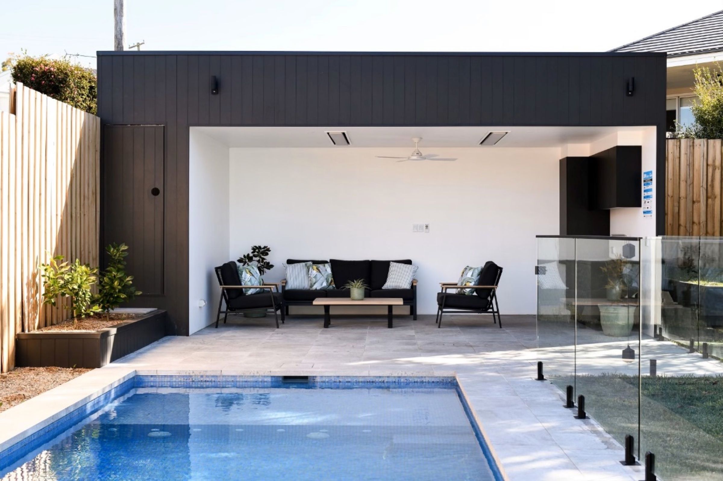 Dark clad pool cabana with an open lounge area beside a tiled pool